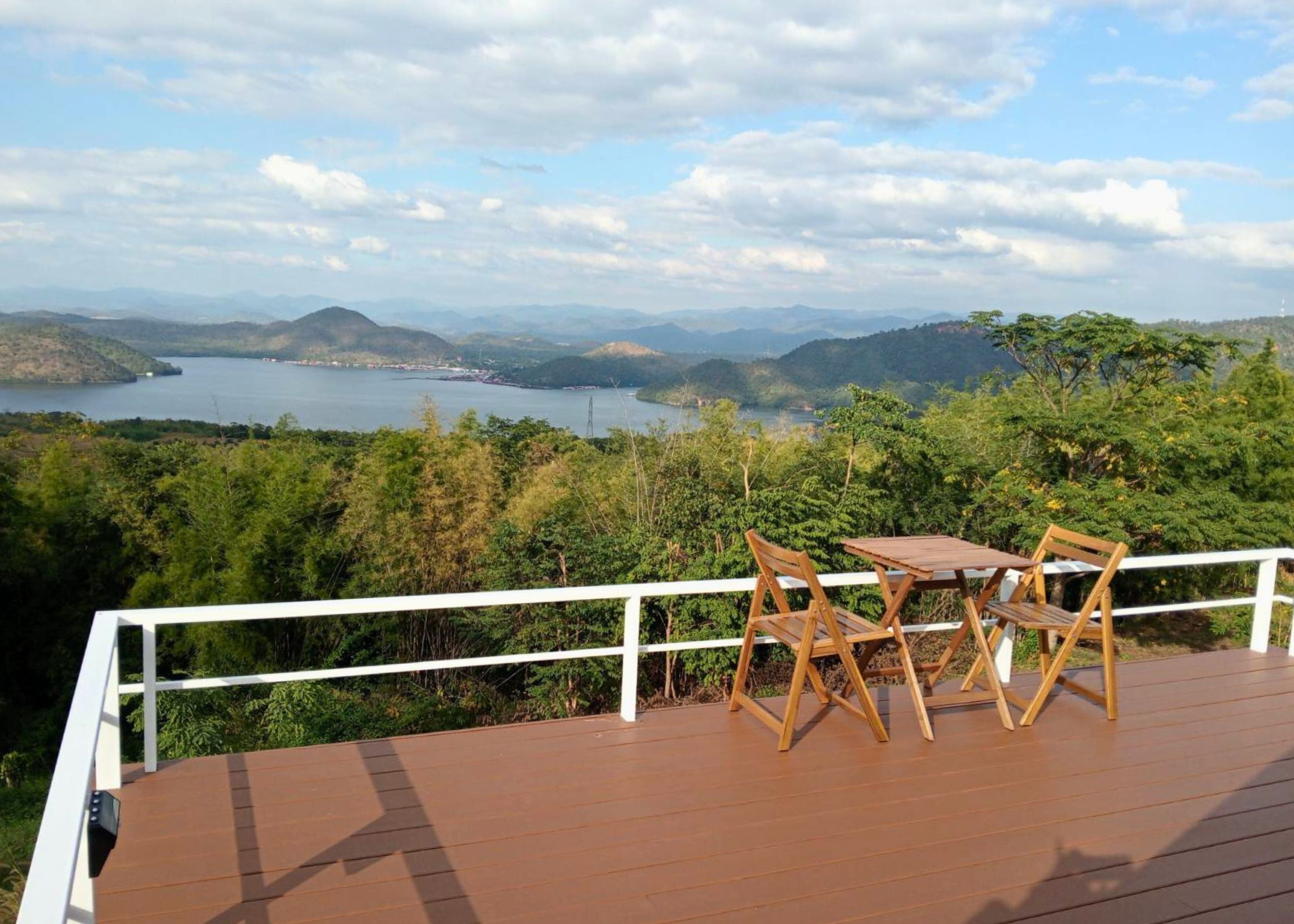 A wooden deck with a table and chairs overlooking a lake and mountains.