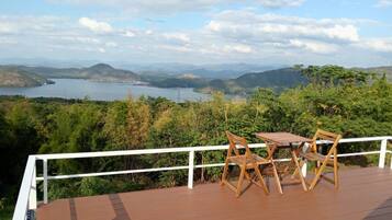 A wooden deck with a table and chairs overlooking a lake and mountains.