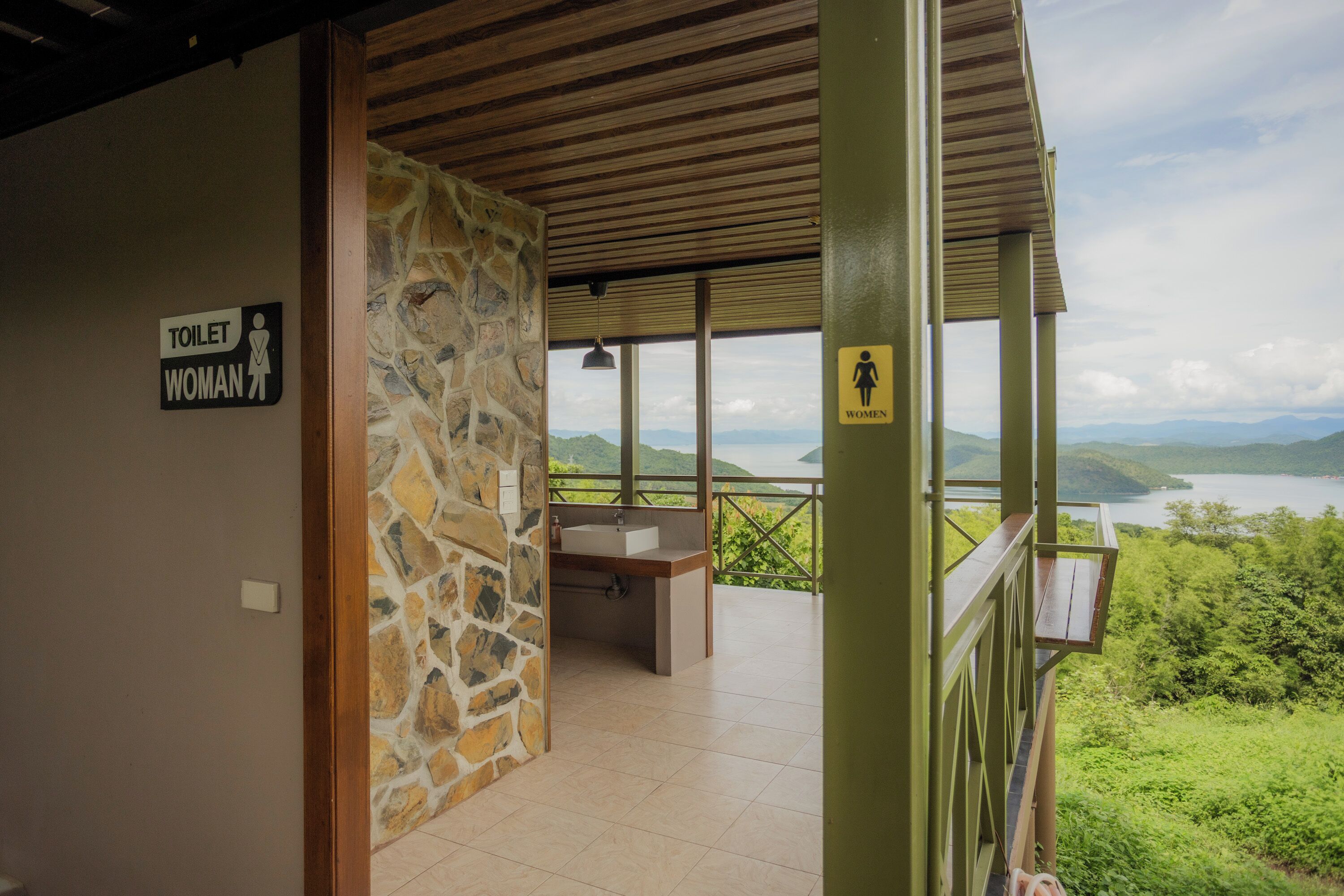 A women's restroom with a stone wall and a view of a lake and mountains.