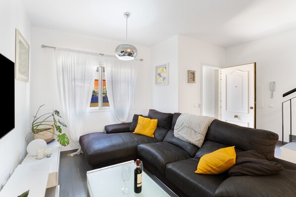A living room with a sofa, a coffee table with a bottle and glass, a potted plant, and a door.