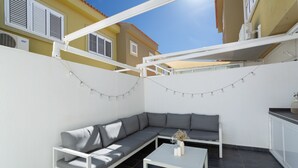 Un espacio exterior moderno con un sofá seccional gris, una mesa de centro blanca y luces colgantes.