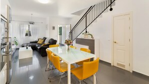 Una sala de estar moderna con una mesa de comedor de vidrio, sillas amarillas, un sofá negro y una escalera.
