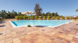 Una piscina con suelo de baldosas, sombrillas y sillas de descanso.