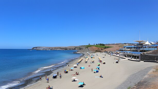 Una playa con sombrillas, gente y edificios al fondo.