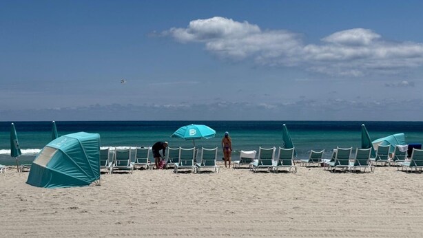 A beach with rows of beach chairs and umbrellas, a tent, and a clear view of the ocean.