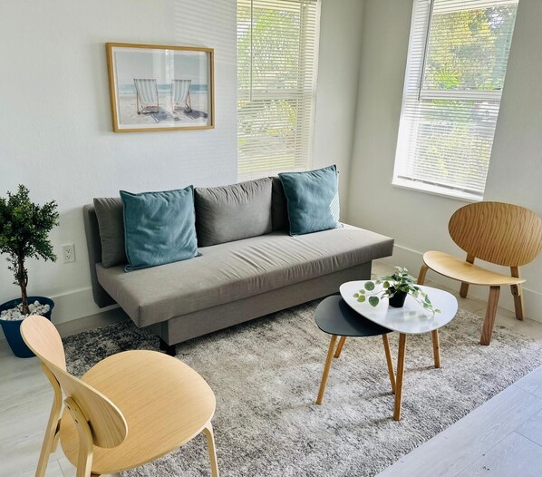 A modern living room with a grey sofa, two teal cushions, a round coffee table, and a wooden chair.