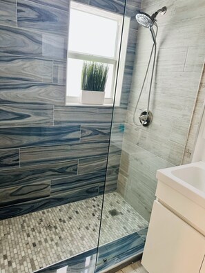 A modern bathroom with a glass shower enclosure, a potted plant, and a toilet.