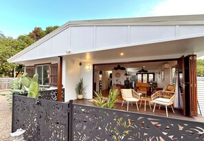 A covered outdoor seating area with chairs and a table, a potted plant, and a view of the interior. - Vila Paus (Urangan)