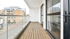 Un balcon doté d’un plancher en bois, de grandes fenêtres et offrant une vue sur une rue de la ville.