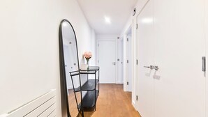 Un couloir avec un miroir à cadre noir, une table ornée d’un vase de fleurs et des portes blanches.