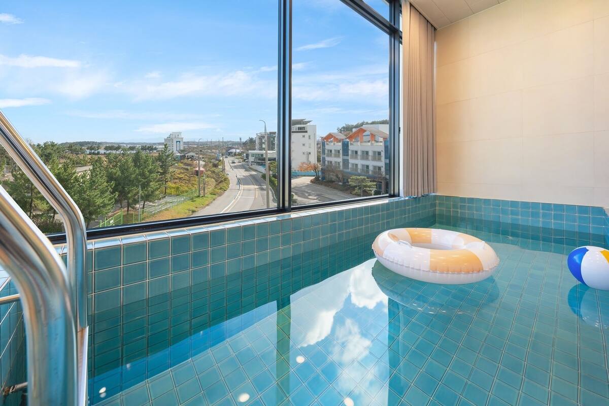 A modern indoor swimming pool with a clear view of the surrounding area through large windows.