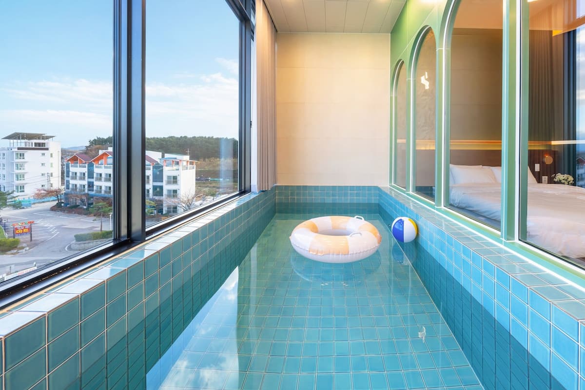 A hotel room with a small indoor pool, a bed, and a view of the cityscape.