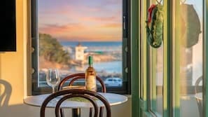 A table with a bottle and glass, a view of the sea, and a green door.