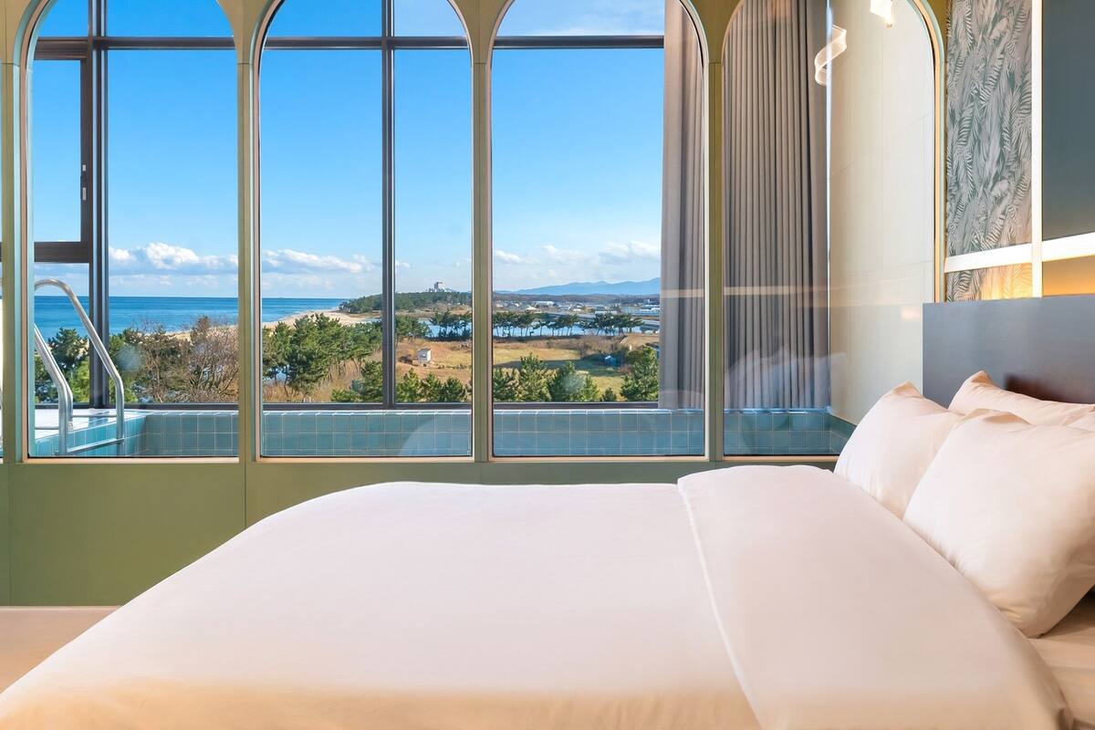 A hotel room with a large bed, a view of the sea and landscape, and a balcony with a pool.