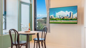 Ein Zimmer mit Tisch, zwei Stühlen, einer Champagnerflasche und einem Fernseher, der eine Stadtansicht zeigt.