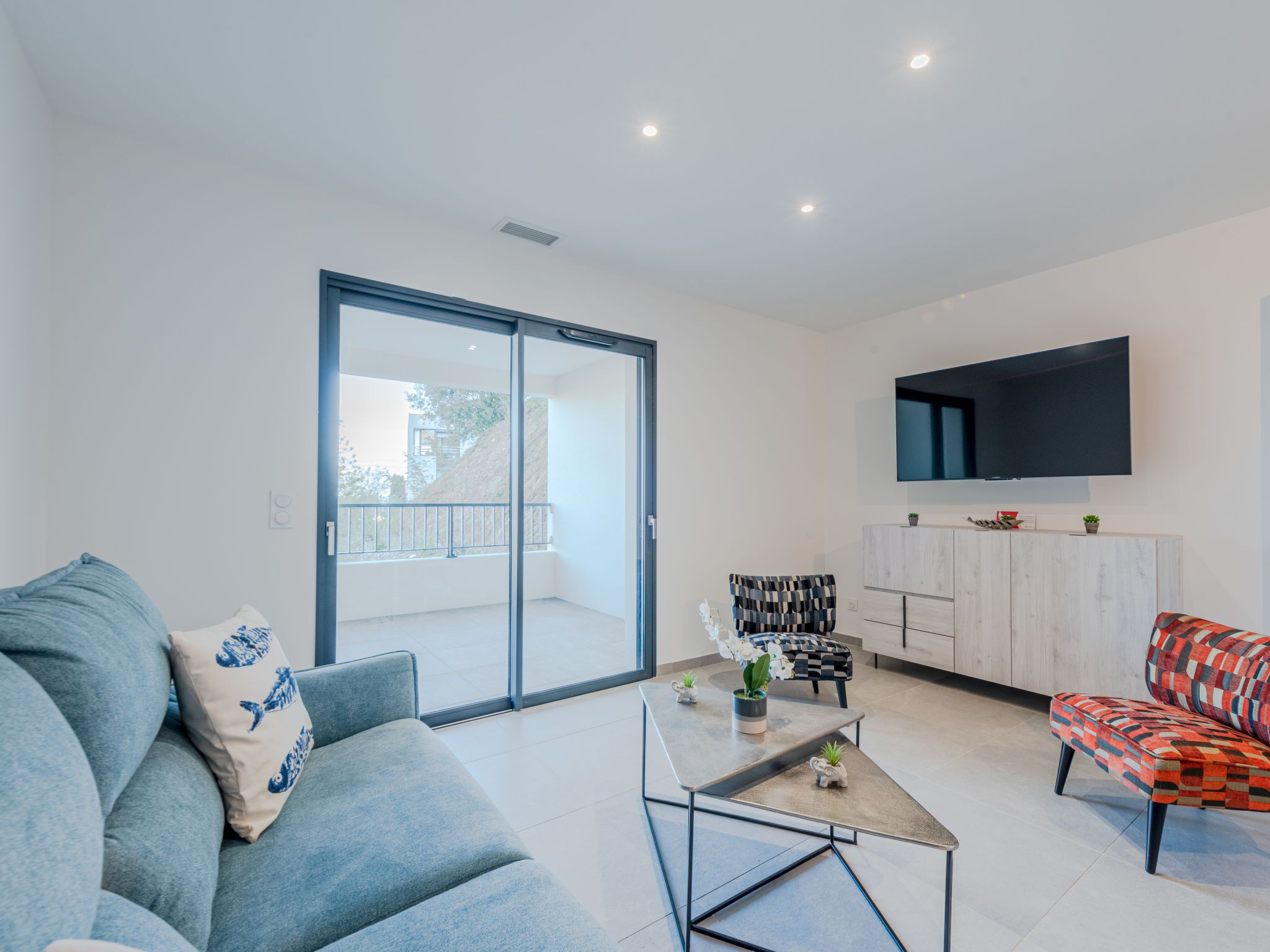 A modern living room with a sofa, armchair, coffee table, and a TV mounted on the wall.