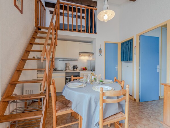 A dining area with a table set for two, wooden chairs, a staircase, and a kitchen in the background. - Les Casellas by Interhome (Saint Cyprien)