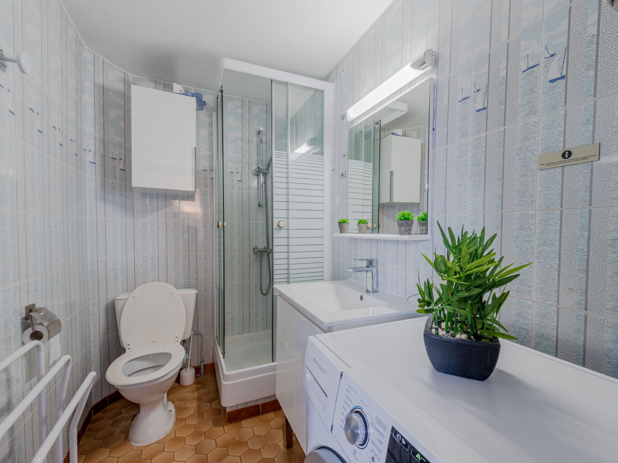 Un baño moderno con ducha acristalada, inodoro, lavamanos y lavadora.
