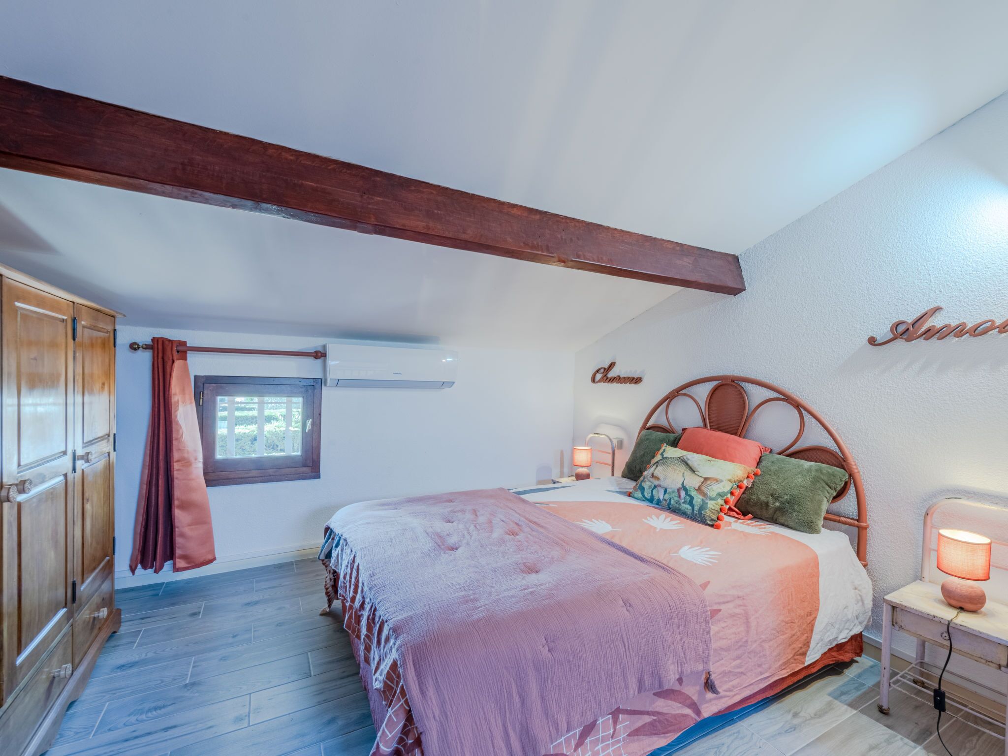 Une chambre à coucher avec un lit en bois, une fenêtre avec des rideaux, un appareil de climatisation et une lampe fixée au mur.