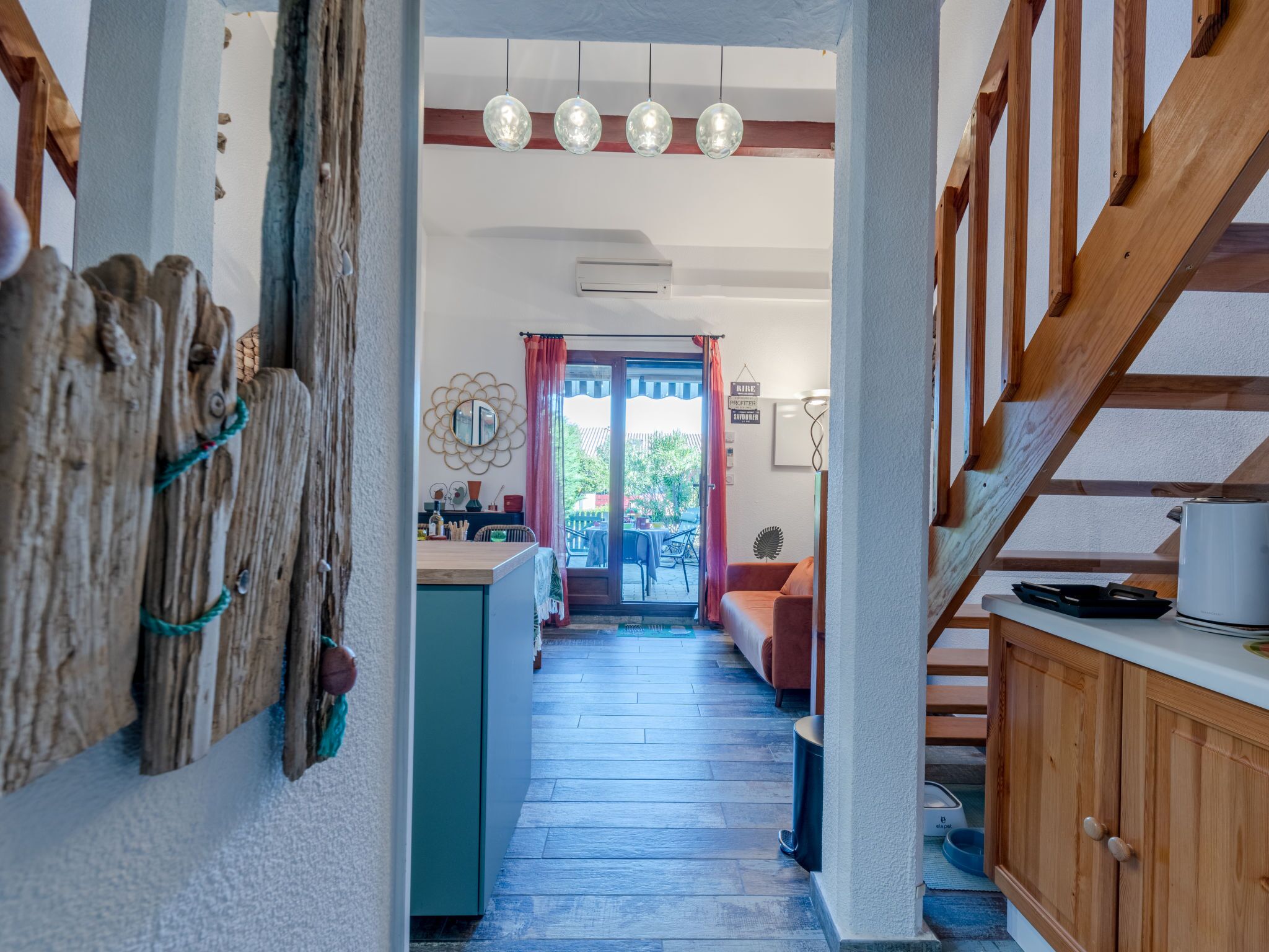 A hallway with a wooden staircase, a kitchen area with a dining table, and a view of the outside.
