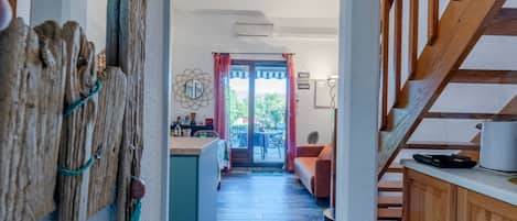 A hallway with a wooden staircase, a kitchen area with a dining table, and a view of the outside.