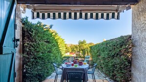 Un patio al aire libre con una mesa lista para comer, rodeado de vegetación y una pérgola arriba.