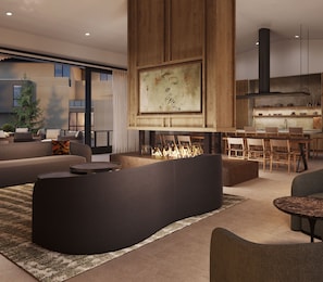 A modern living room with a curved black sofa, a fireplace, a dining area with wooden chairs, and a kitchen with a large window.