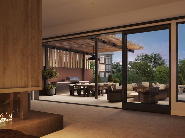 Une terrasse extérieure moderne, dotée d’un barbecue, d’un espace salon et de grandes portes-fenêtres coulissantes donnant accès à un bâtiment.