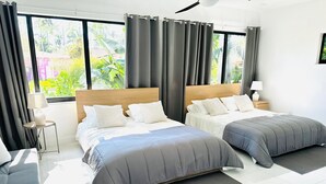 Moderni hotellihuone, jossa on kaksi sänkyä, sohva, pieni pöytä ja yöpöytä.