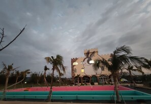 Experience the unique architecture of this hotel, featuring a striking tower and vibrant mural of a rabbit on its facade, surrounded by lush palm trees and a colorful pool area.