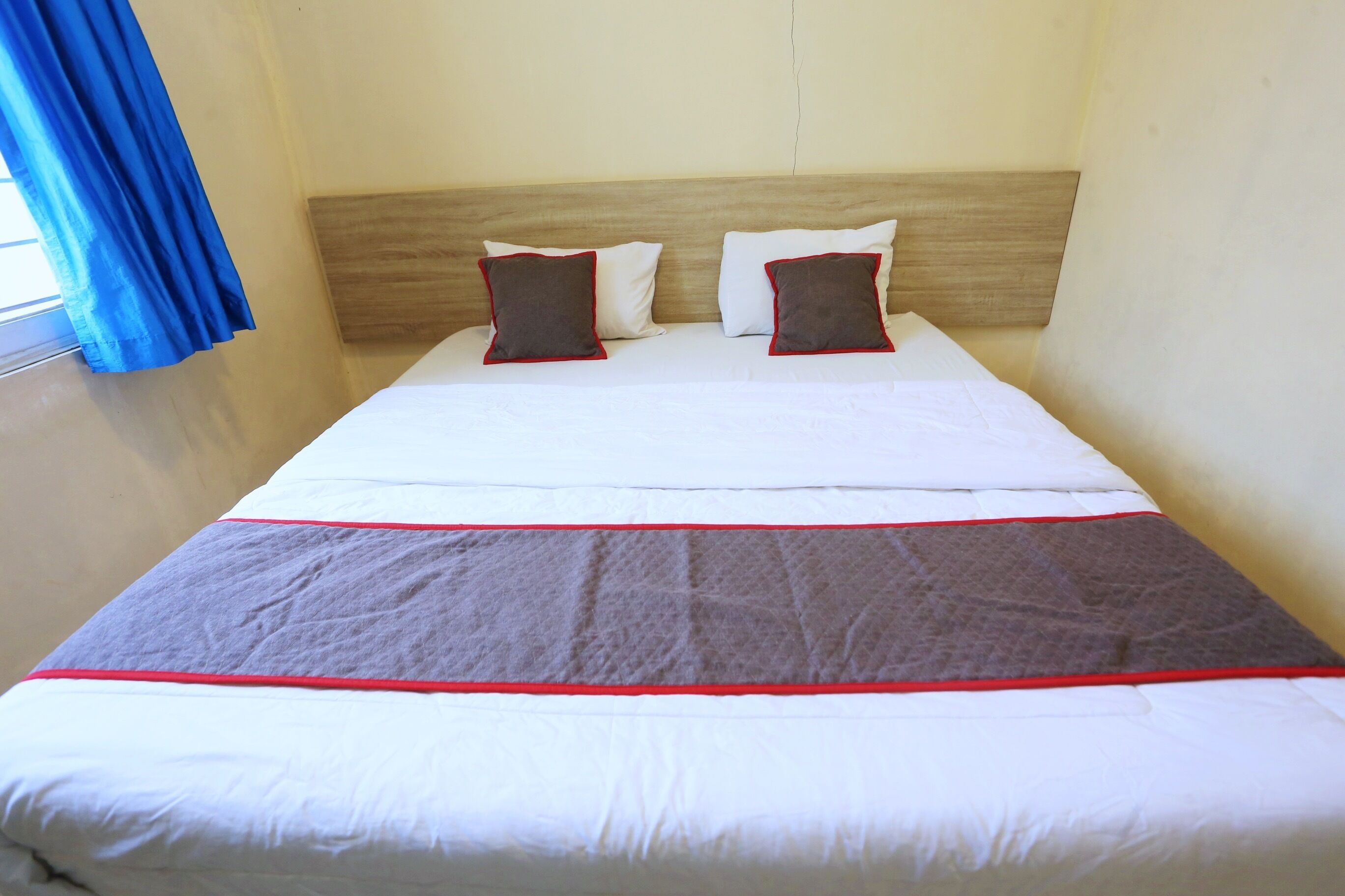 Een hotelkamer met een bed, twee kussens, een hoofdbord en een raam met blauwe gordijnen.