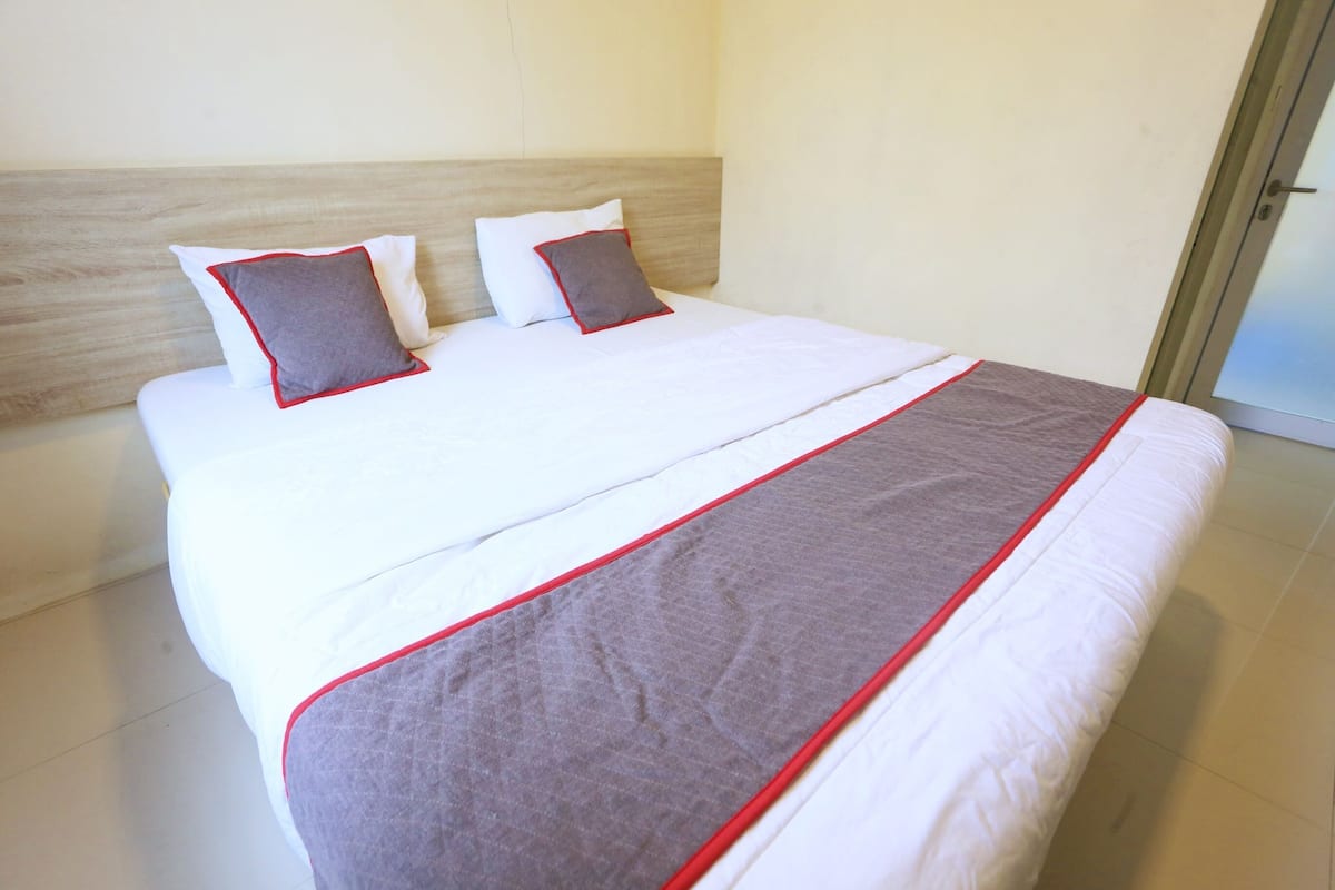A neatly made bed with white bedding and a gray and red accent blanket.