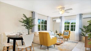 A modern living room with a dining area, featuring a sofa, armchairs, a coffee table, and a dining table set for four.