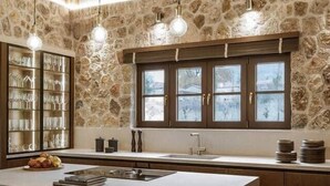 A kitchen with a stone wall, wooden beams, a large island with bar stools, and pendant lighting.