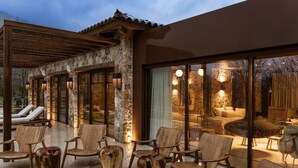 A modern outdoor lounge area with stone walls, wooden furniture, and large windows.