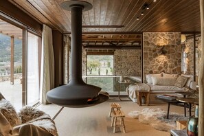 A cozy interior with a stone wall, a fireplace, a sofa, and a view of the outdoors.