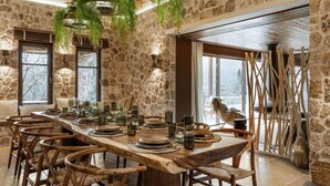 A stone-walled dining area with a long wooden table set for a meal, surrounded by wicker chairs.