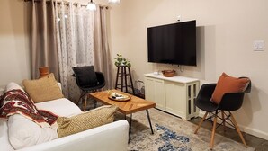 Ein Wohnzimmer mit einer Couch, zwei Sesseln, einem Couchtisch, einem Fernseher und einer Pflanze.