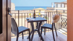 A balcony with a table, two chairs, a bottle of wine, and a glass of wine. The view includes a building and a clear sky. - Pirandello by Interhome (Balestrate)