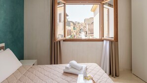 A hotel room with a bed, a window with curtains, and a view of a cityscape.