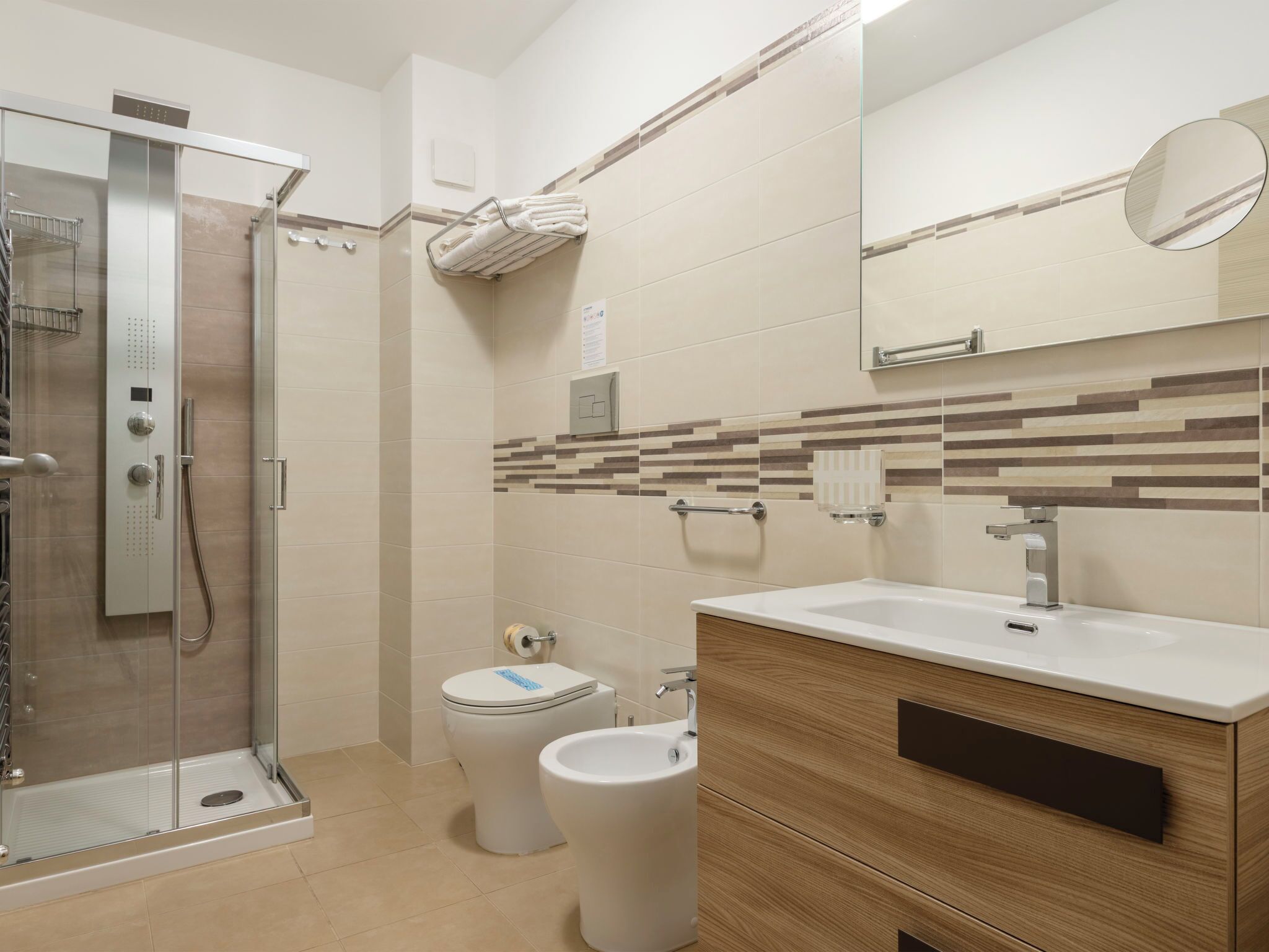 Ein modernes Badezimmer mit einer Duschkabine, einer Toilette, einem Bidet und einem Waschtisch mit Spiegel.