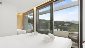 A modern bedroom with a large bed, a view of the city, and a balcony with a chair. - Villa Kolibri | Mountain view - pool - garden (La Cala de Mijas)