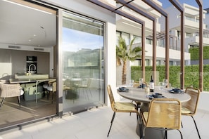 A modern outdoor dining area with a glass wall, wicker chairs, and a table set for two. - Mijas Villa w/ Private Pool & Panoramic Mountain (La Cala de Mijas)