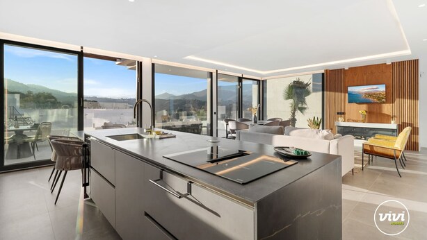 A modern kitchen with a large island, a dining area with a yellow chair, and a TV mounted on a wooden panel. - Villa Kolibri | Mountain view - pool - garden (La Cala de Mijas)
