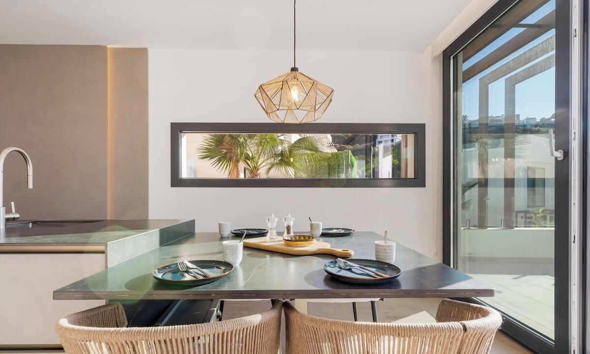 Una cocina moderna con una isla de vidrio, sillas de comedor y una lámpara colgante.