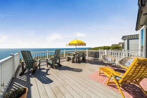 Een terras met tuinmeubilair, een gele parasol en uitzicht op de oceaan.