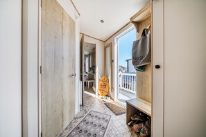 Een gang met een houten deur, een uitzicht op een balkon met een surfboard, en een schoenenrek.