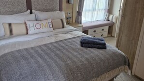 A neatly made bed with a patterned bedspread and pillows, a bedside table with a lamp, and a window with curtains. - SeaView,Sleeps 4to6,Pet friendly, Parking (Wareham)