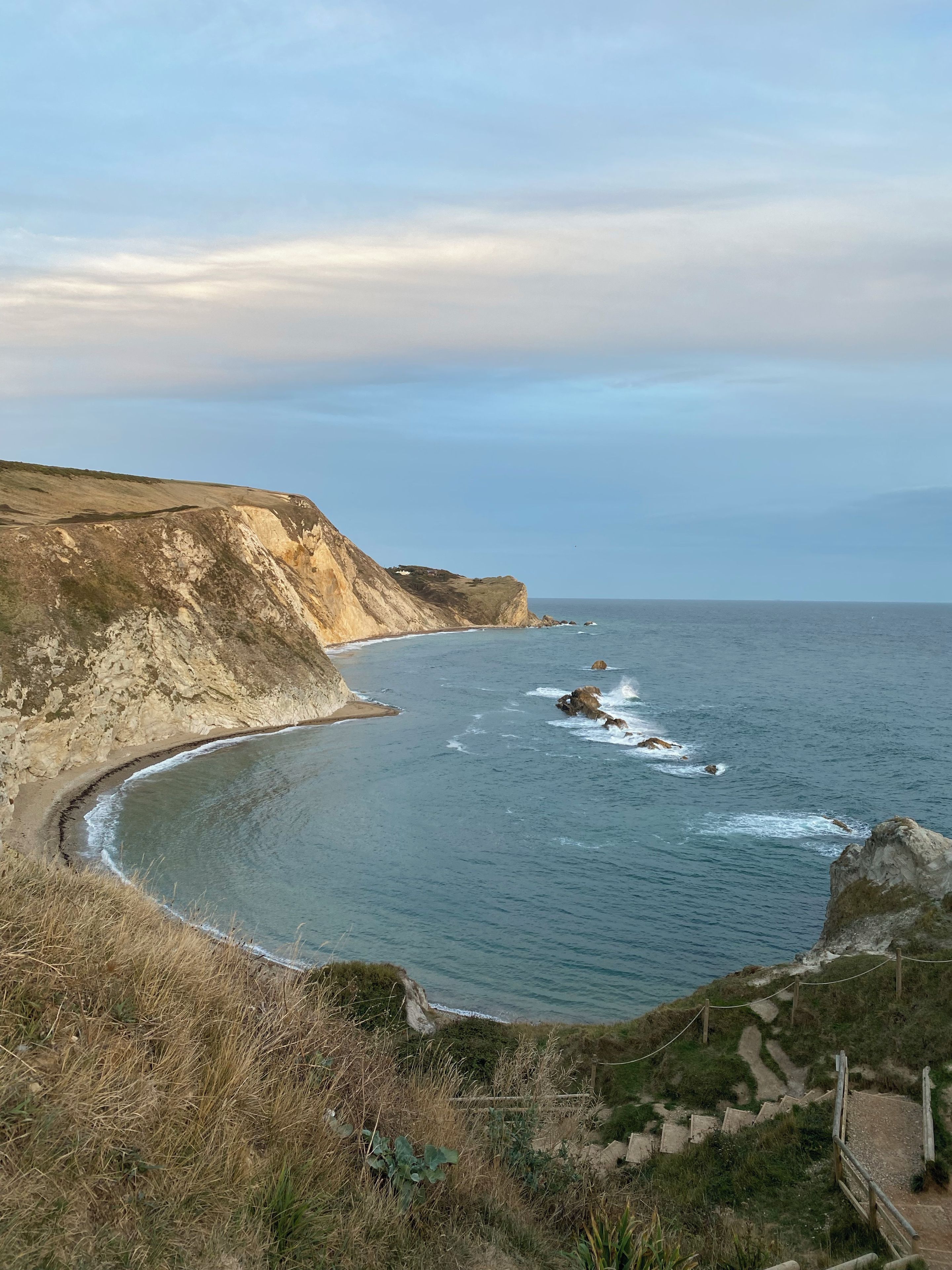 A coastal landscape with a curved beach, rocky cliffs, and a clear sky.