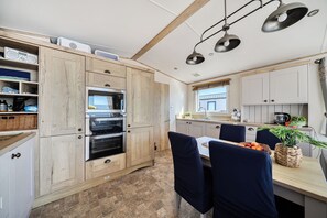 Een moderne keuken met houten kastjes, een inbouwoven en een eethoek met een tafel gedekt voor twee personen.
